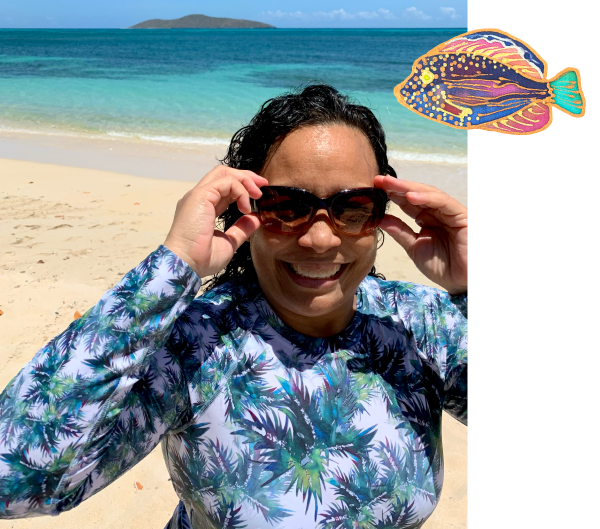 Debbie at the beach wearing palm leaf wetsuit and sunglasses with watercolor fish graphic