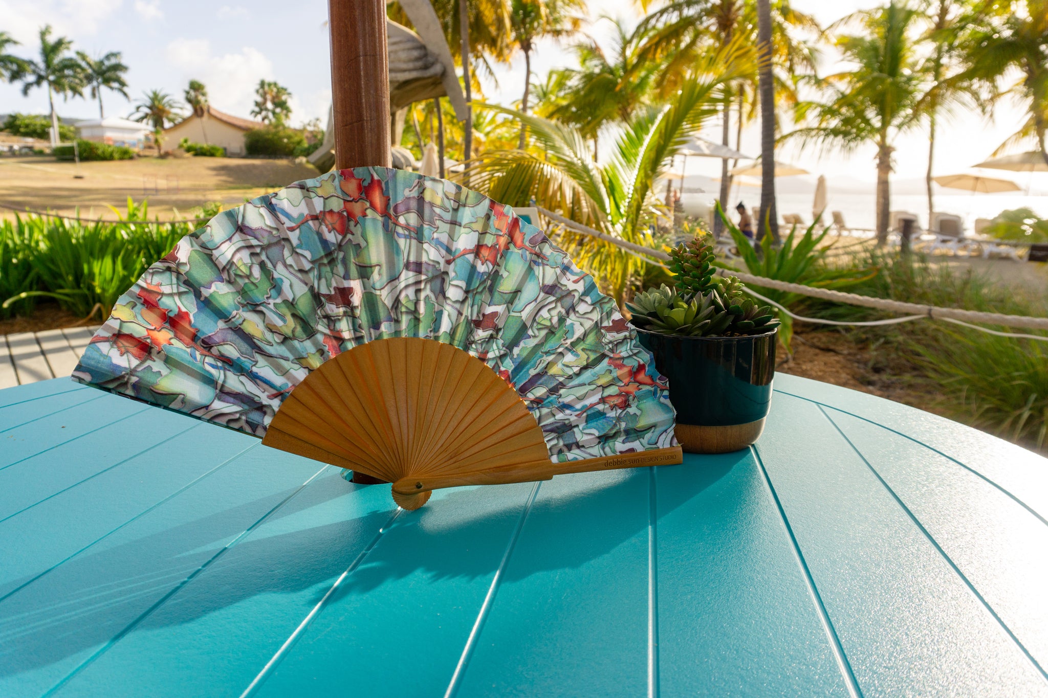 Watercolor floral leaf art hand fan on blue table at the beach
