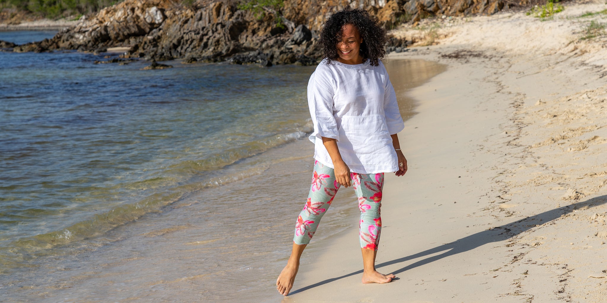 Woman on the beach with pink and turquoise floral leggings and white tunic top